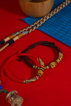Tibetan Vajra knot red string hand-knotted protection sacred cord bracelet — macro stone texture | BuddhaManifest™